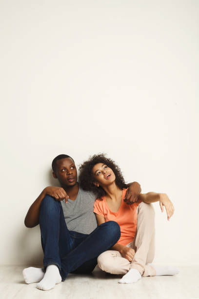 istock African-american couple looking up, sitting on floor 909488680
