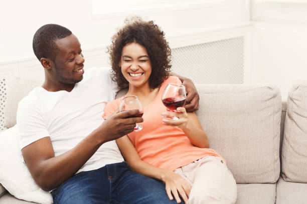 istock Smiling black couple drinking wine on sofa at home 909494012