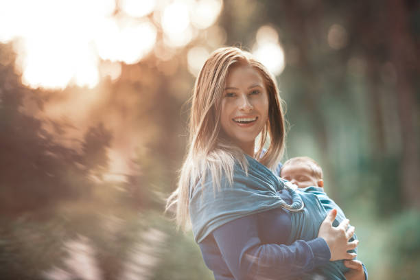 walking in beautiful day with her daughter lifestyle shot of young woman walking eith her baby girl in the nature. baby carrier stock pictures, royalty-free photos & images