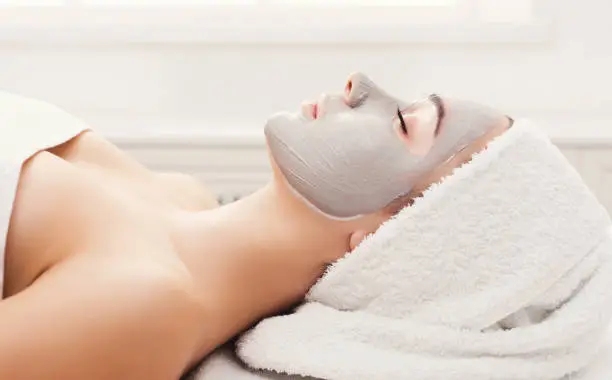 Face mask, spa beauty treatment. Woman applying facial clay mask at spa salon, skincare, side vies