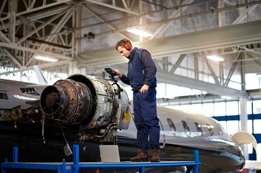 Aircraft engineer in the hangar repairing and maintaining airplane jet engine.