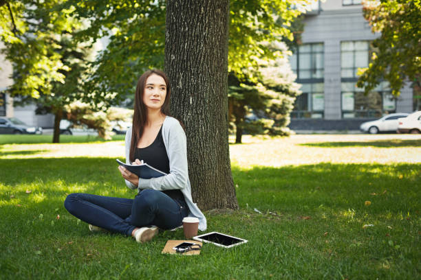 istock Young woman sitting with notebook on grass 909519284