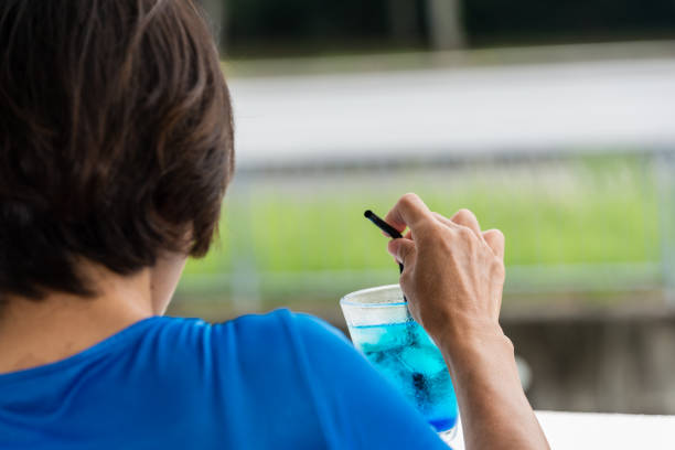 A Japanese lady sitting an outside bar overlooking some scenery while partaking in colorful beverages containing alcohol and fruit juices and