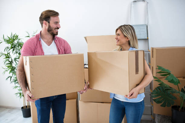 istock Smiling young couple holding boxes and packing for moving 909535156