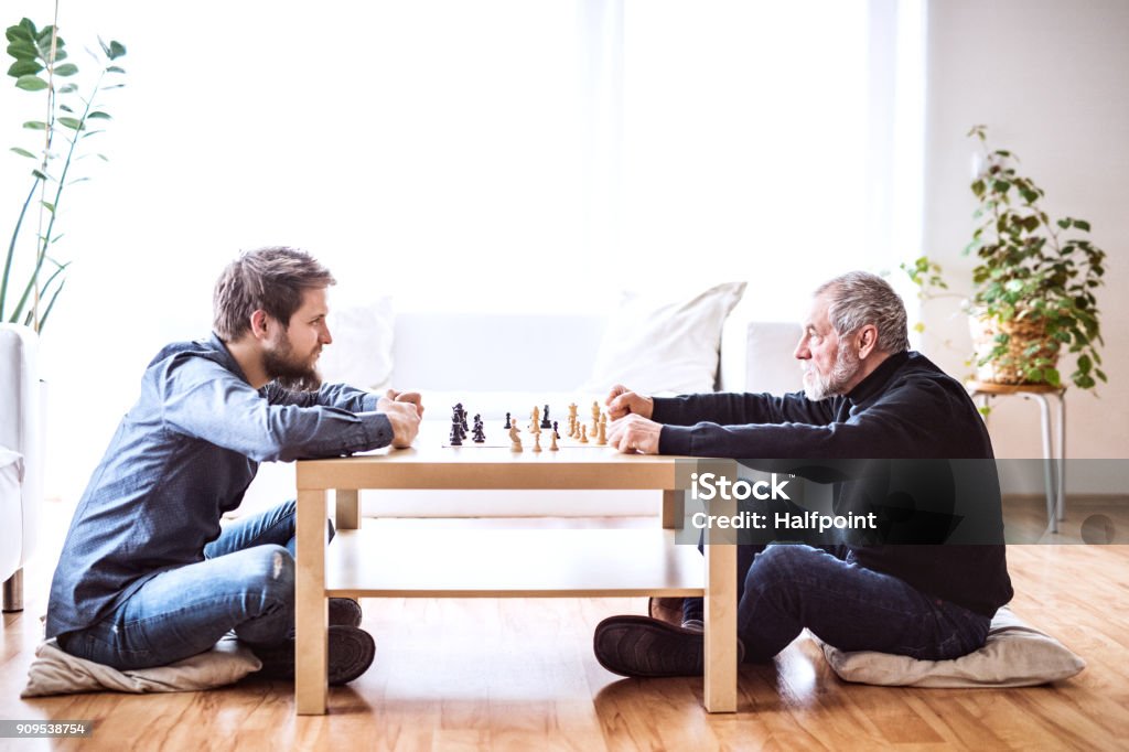 Hipster son and his senior father at home. Hipster son and his senior father at home, playing chess. Two generations indoors. Chess Stock Photo