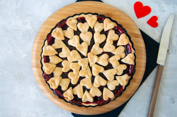istock Cherry pie with heart shape decorations from flaky dough on a white backdrop 909538998