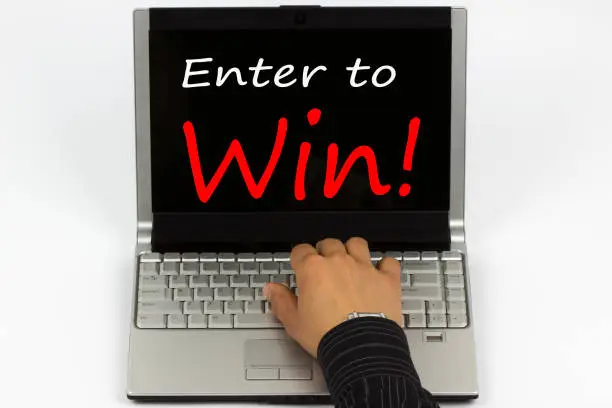 Enter to Win! written on laptop screen.Hand of a man on a keyboard.