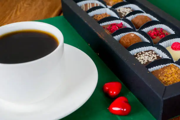 delicious chocolate candies in gift box with coffee cup and two red hearts, close-up shot