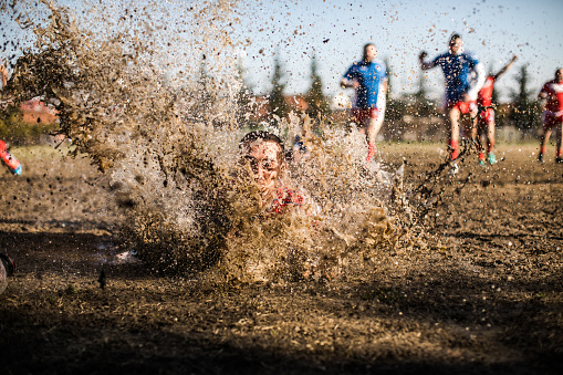 Group of men playing rugby outdoors,one of them falling in mud and splashing