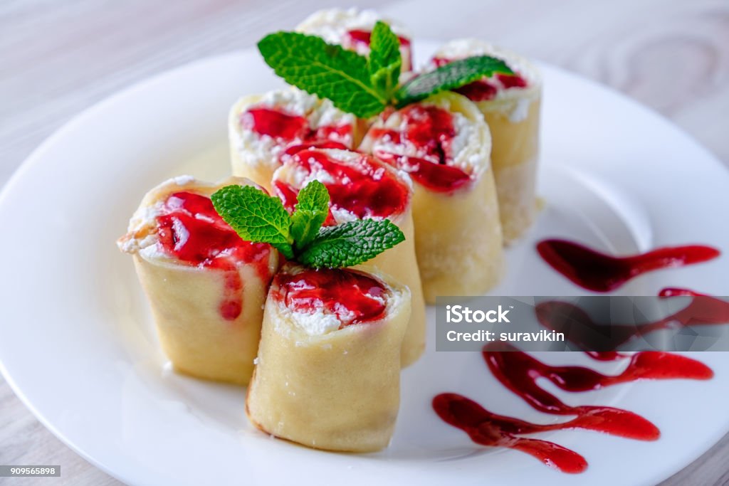 Pancakes stuffed with cottage cheese on a white plate. Pancakes stuffed with cottage cheese on a white plate, poured with jam and decorated with green mint leaves. Rolling Stock Photo