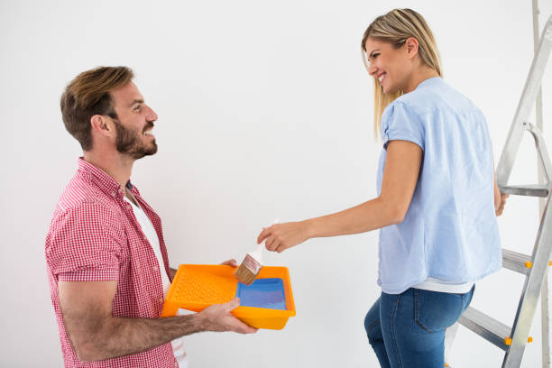 istock Young smiling couple painting walls 909573370