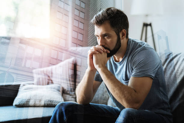Thoughtful serious man sitting and thinking Think about it. Thoughtful serious beardful man sitting in the empty room holding hands near mouth and thinking. man regret stock pictures, royalty-free photos & images