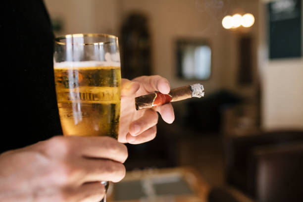 istock Close Up Of Man Smoking Cigar While Holding A Beer 909574778