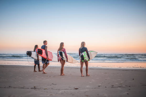 istock Young surfers walking on the beach at sunrise 909575012