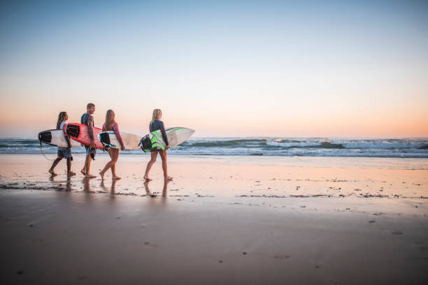 istock Young surfers walking on the beach at sunrise 909575046