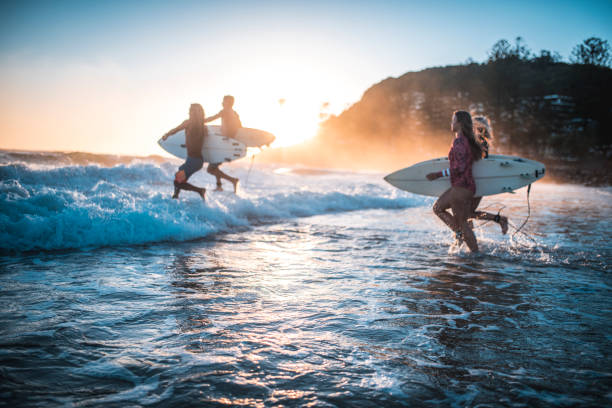 amici che corrono nell'oceano con le loro tavole da surf - frangente foto e immagini stock