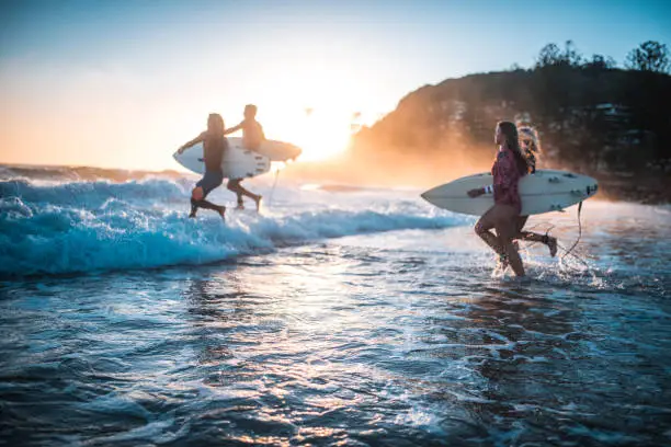 Photo of Friends running into the ocean with their surfboards