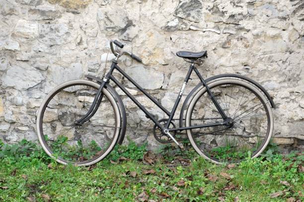 istock Old bike standing on grass in front of old stone wall 909634420