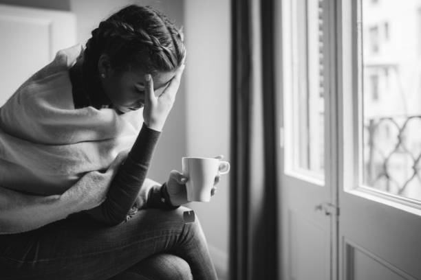 Depressed woman at home Unhappy woman sitting at the bed with cup of tea headache menstruation pain cramp stock pictures, royalty-free photos & images