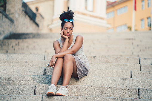 Unhappy young girl sitting at the steps outside