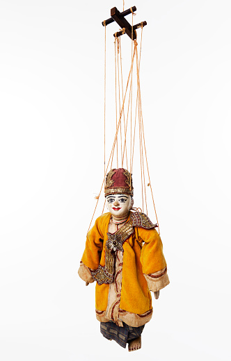 Suspended by wires ancient Asian wooden marionette representing a man. Dressed in traditional clothes. Studio photo, white background.