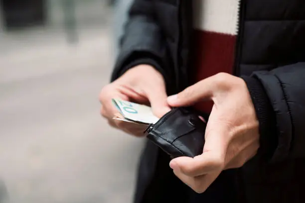 closeup of a young caucasian man on the street putting in or taking off euro banknotes from a wallet