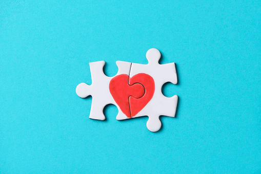 closeup of two pieces of a puzzle forming a heart, depicting the idea that love is a matter of two, on a blue background, with some blank space around it
