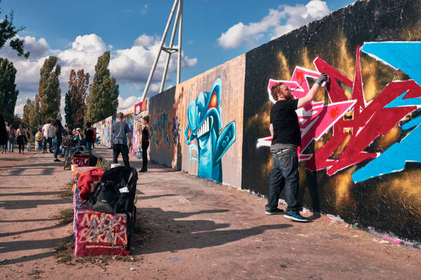 Close-up view of a street artist's hand skillfully holding a spray can, creating a vibrant mural filled with color on an urban wall