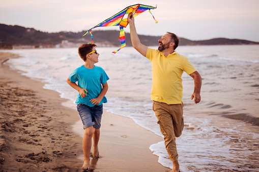 Photo of father and son having fun with a kite on the beach