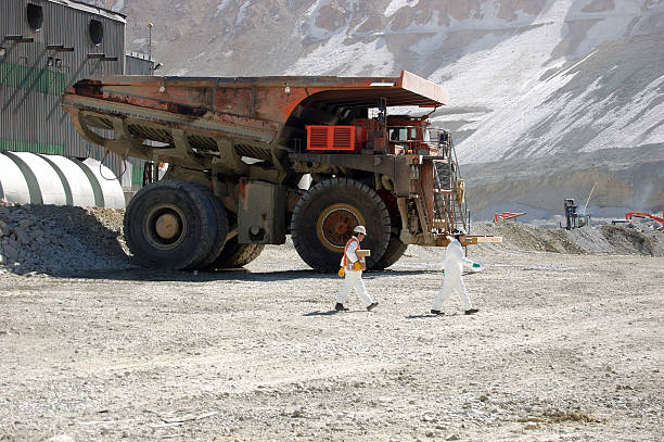 Two miners in white hard hats walk past large mining truck stock photo