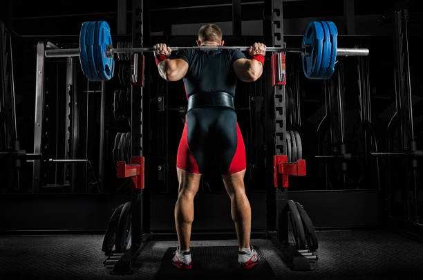 Professional athlete is standing with a barbell on his shoulders and is about to sit down with her. stock photo