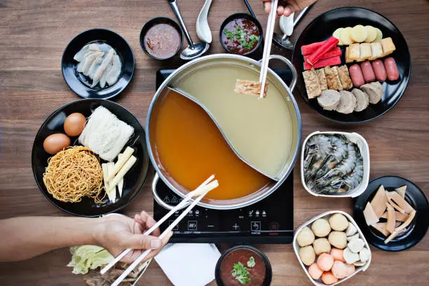 Top down view of a hotpot dinner with a plethora of seafood and deep fry dishes as two person tries to eat