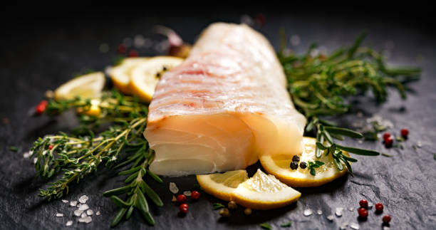 Fresh raw cod fillet with addition of herbs and lemon slices