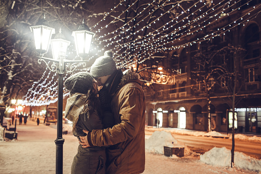 Young couple in love kisses under holiday winter illumination at night