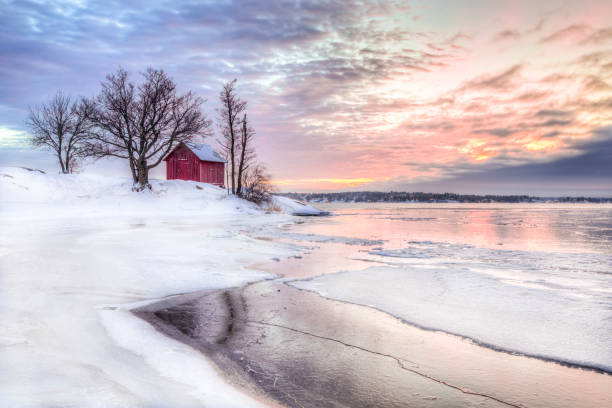 A Red little cottage in Stockholms archipelago A winter photo of a red little cottage with some trees in the archipelago of Stockholm, Sweden. There is snow on the ground and some ice on the lake. The sky is colored from the beautful winter sunset. swedish sauna stock pictures, royalty-free photos & images