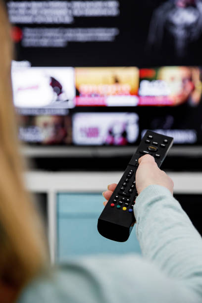 Woman Holding a TV remote control and switching channels on TV set stock photo