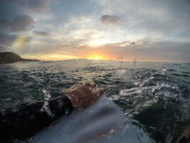istock Surfer holding a surfboard at sunset with water spray (point of view) 909701258