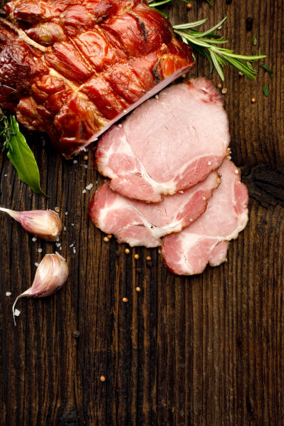 istock Smoked gammon sliced on a wooden rustic table with addition of fresh aromatic herbs, top view 909714558