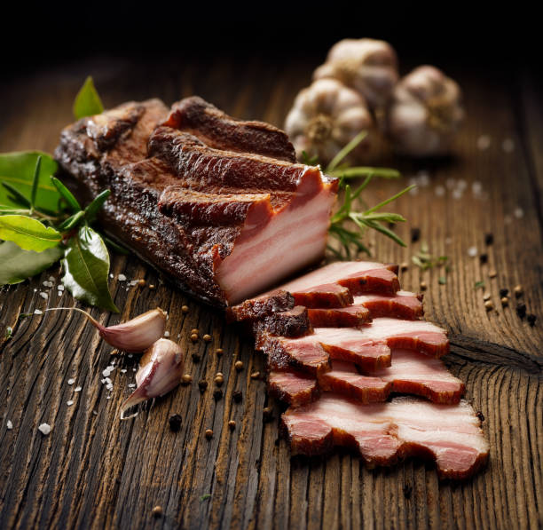 istock Smoked bacon on a wooden rustic table with addition of fresh aromatic herbs 909715312