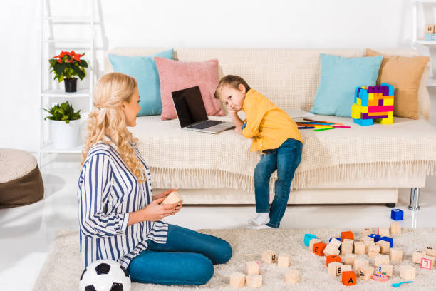 istock little boy using laptop on sofa while mother sitting on floor at home 909715484