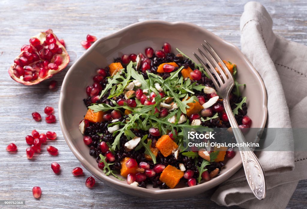 Salad with black rice, baked pumpkin, pomegranate seeds, arugula and nuts on a gray background Salad with black rice, baked pumpkin, pomegranate seeds, arugula and nuts on a gray background. Delicious vegan food Pomegranate Stock Photo