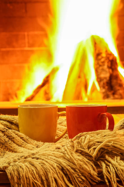 istock Two colorful mugs for tea or coffee, wool things near cozy fireplace . 909756344