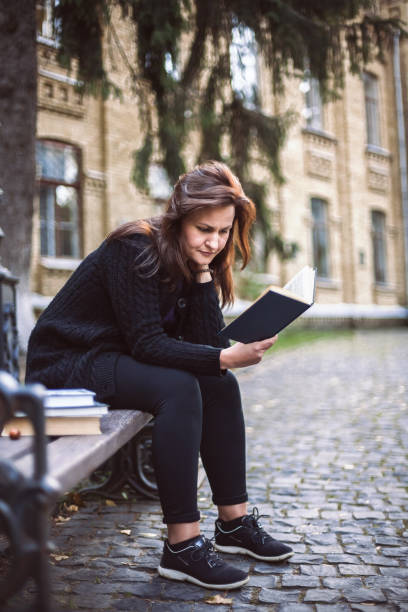 istock Young woman sitting on the bench reading book 909760830