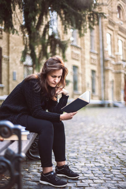 istock Female student sitting on the bench reading book 909760834
