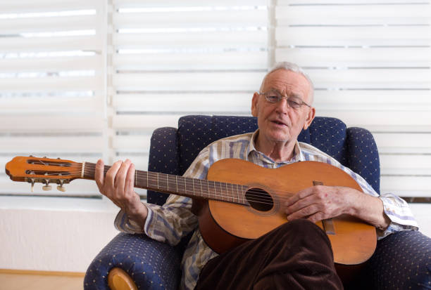 istock Old man playing guitar at home 909761234
