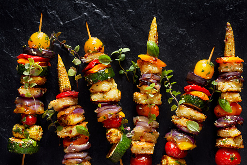 Grilled vegetable skewers with addition halloumi cheese on black background