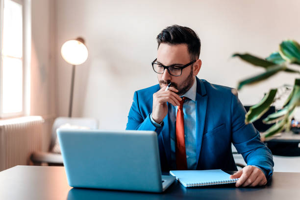 Young manager sitting at desk in bright office, working on laptop.