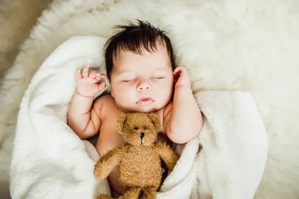 Photo of Newborn baby girl sleeps wrapped in white blanket.