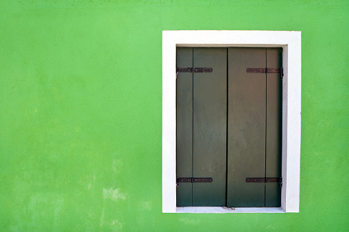 Window with closed green shutter on bright green  wall. Italy, Venice, Burano island.