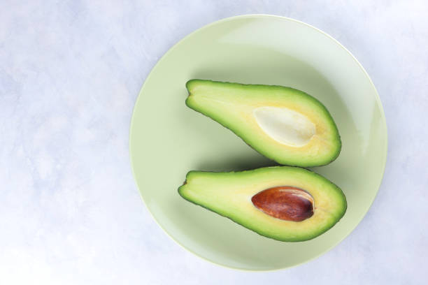 istock Avocado in a green plate on a white background, green fruit, tropical fruit, cut avocado on a marble background, healthy food, vegan, minimalism 909778836